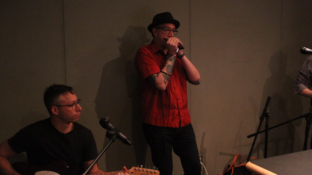 An adult playing guitar and an adult playing harmonica in a radio studio