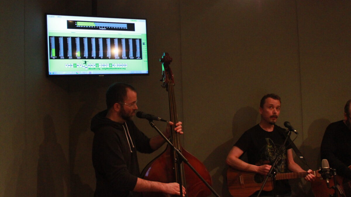 Adult playing upright bass and an adult playing guitar in a radio studio