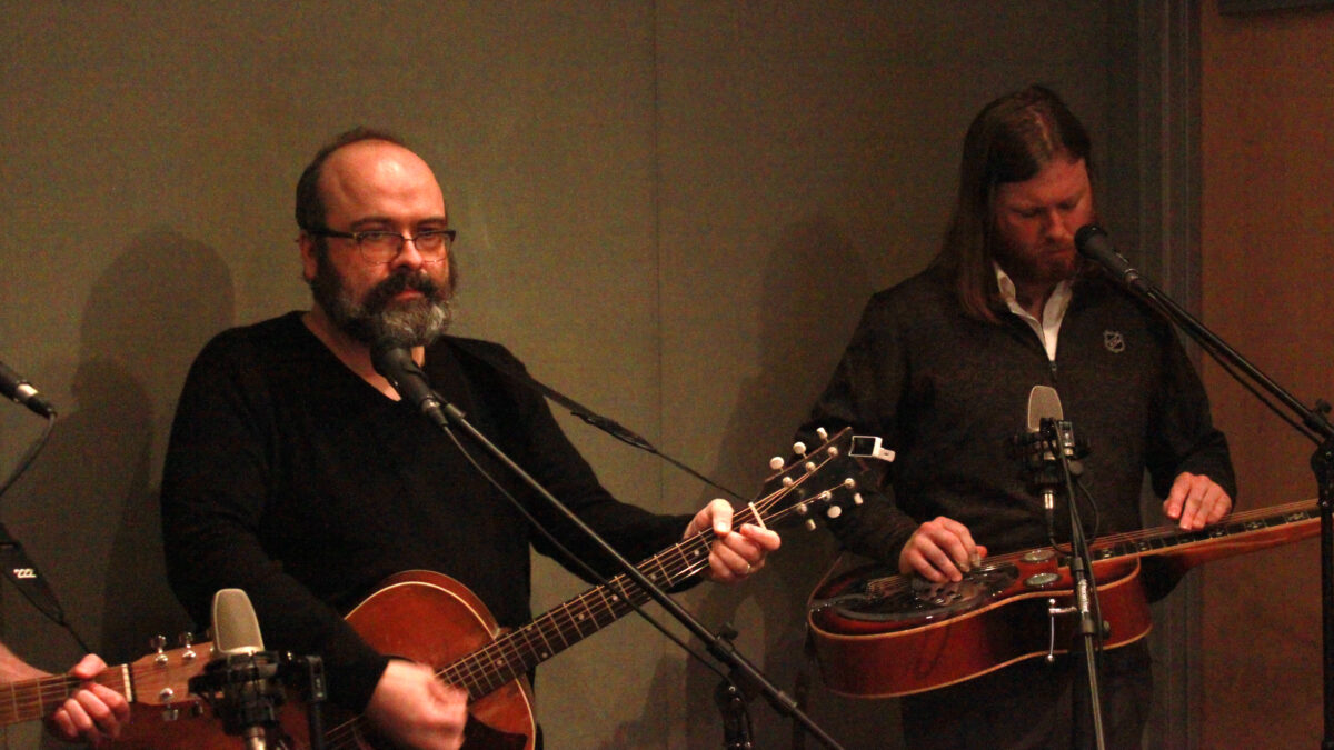 An adult playing guitar and an adult playing a dobro in a radio studio
