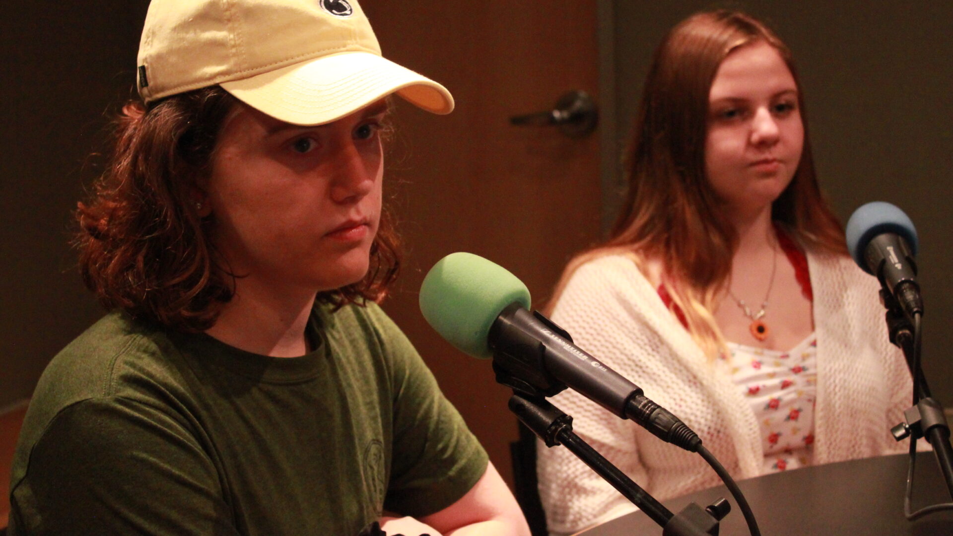 Two teens sitting behind microphones in a radio studio