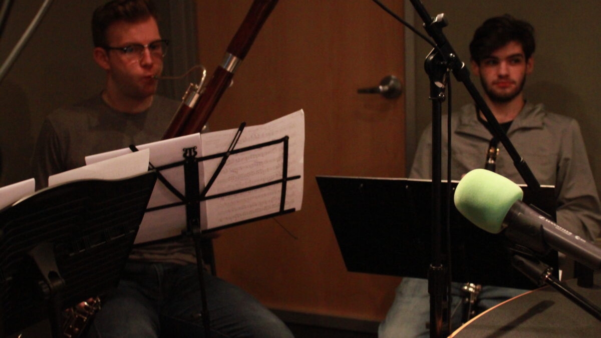 A teen playing a bassoon and a teen holding a clarinet, both looking at sheet music on music stands in a radio studio