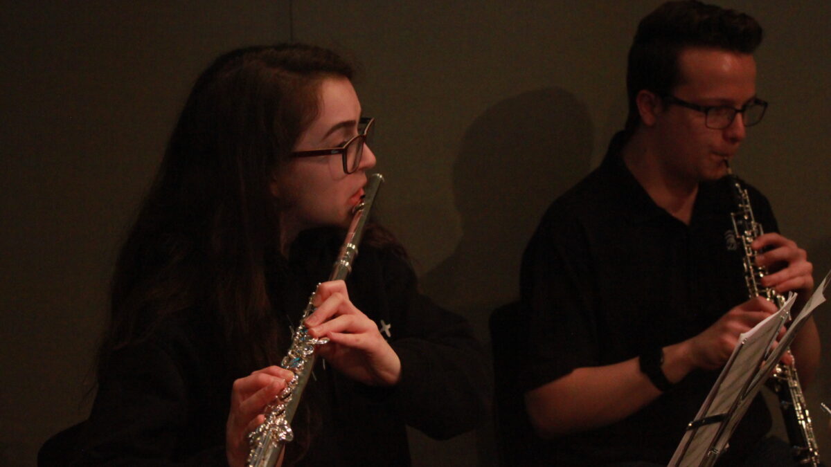 A teen playing flute and a teen playing oboe, both looking at sheet music on music stands in a radio studio
