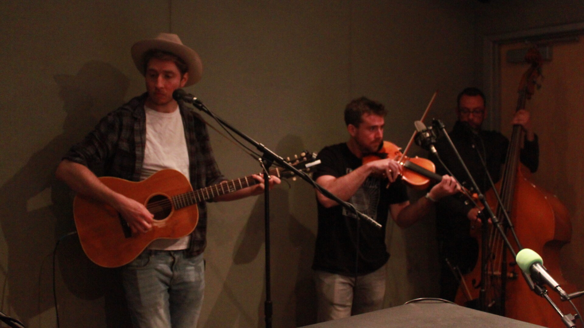 An adult playing guitar, an adult playing violin, and an adult playing upright bass in a radio studio