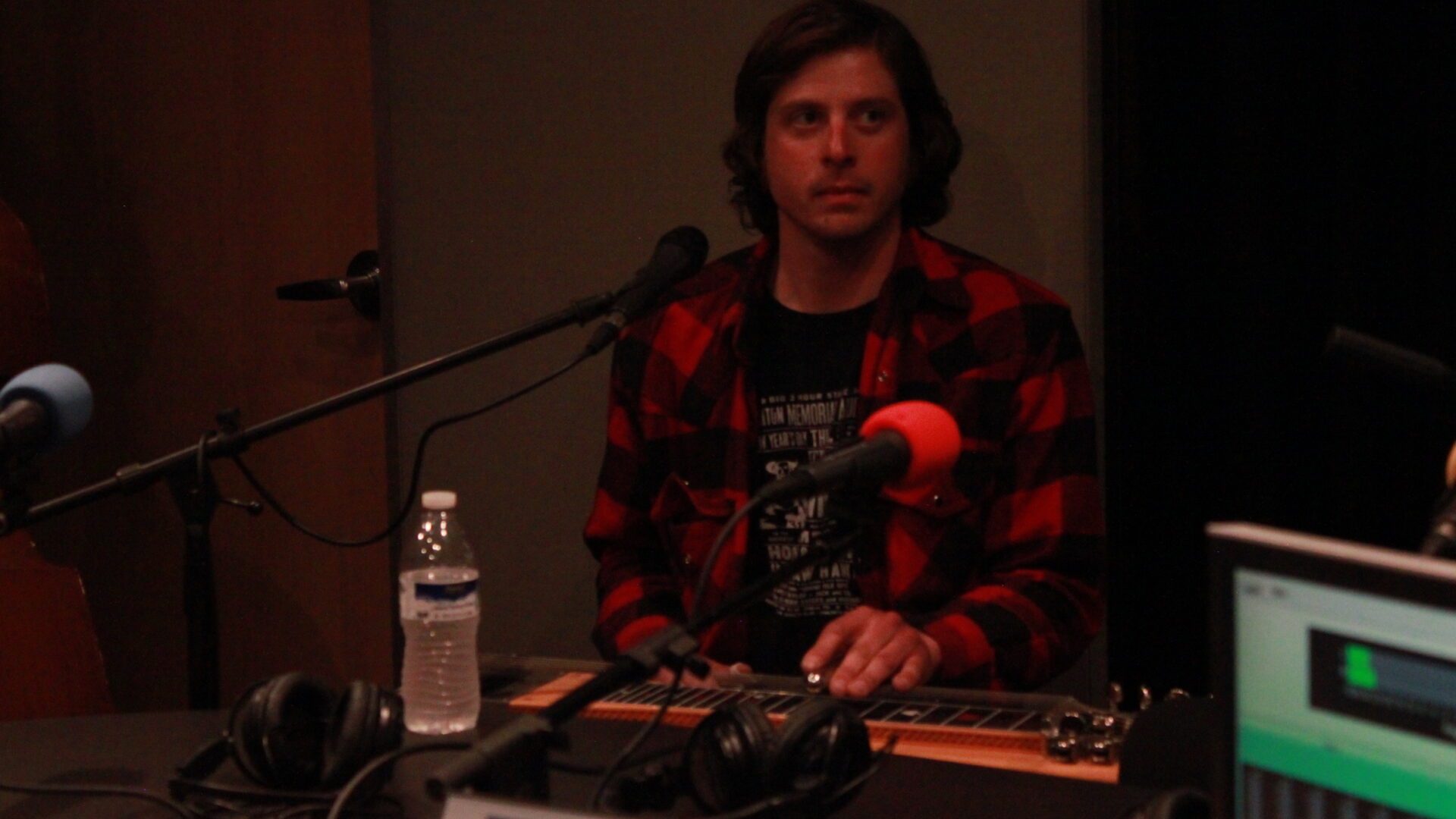 Adult playing a lap guitar sitting behind a microphone in a radio studio