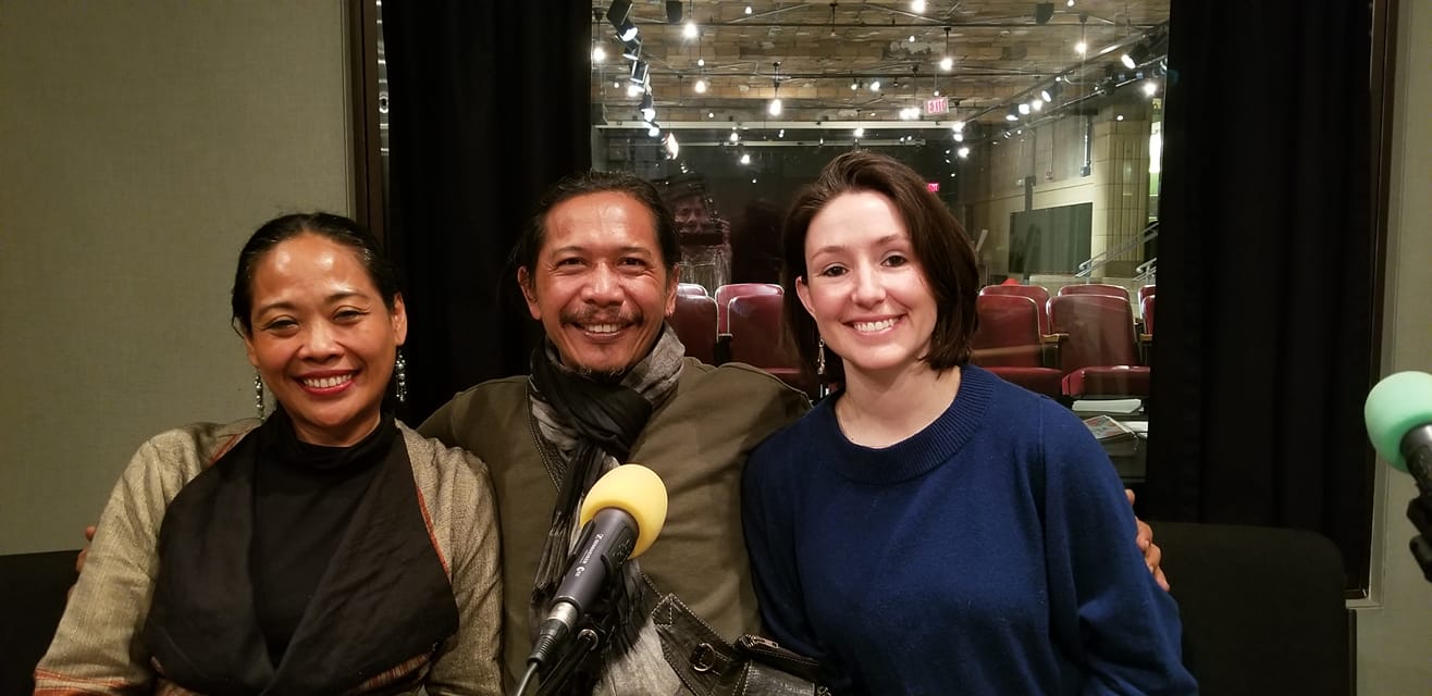 Three adults smiling and posing behind a microphone in a radio studio
