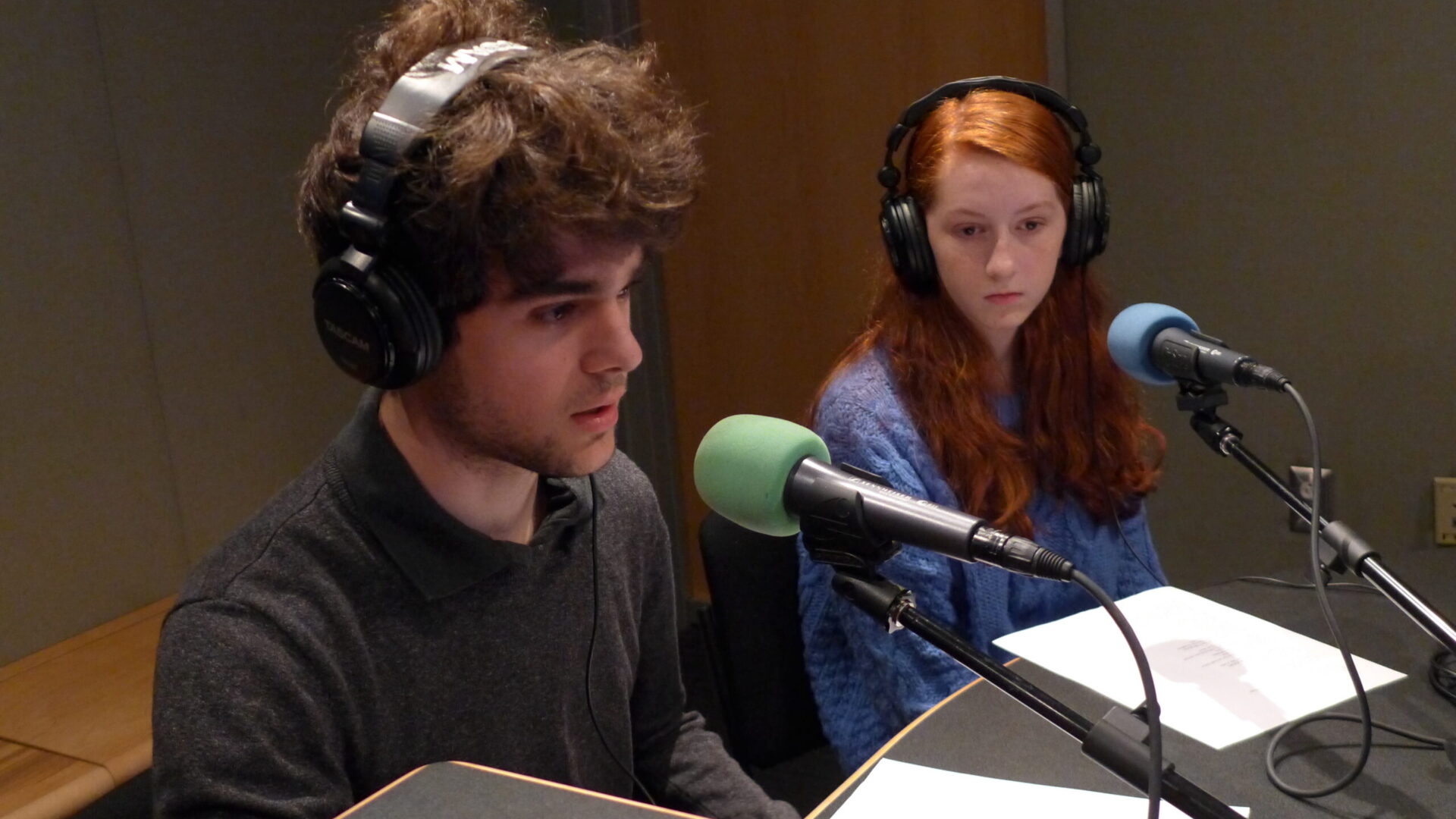 Two teens wearing headphones speaking into microphones in a radio studio
