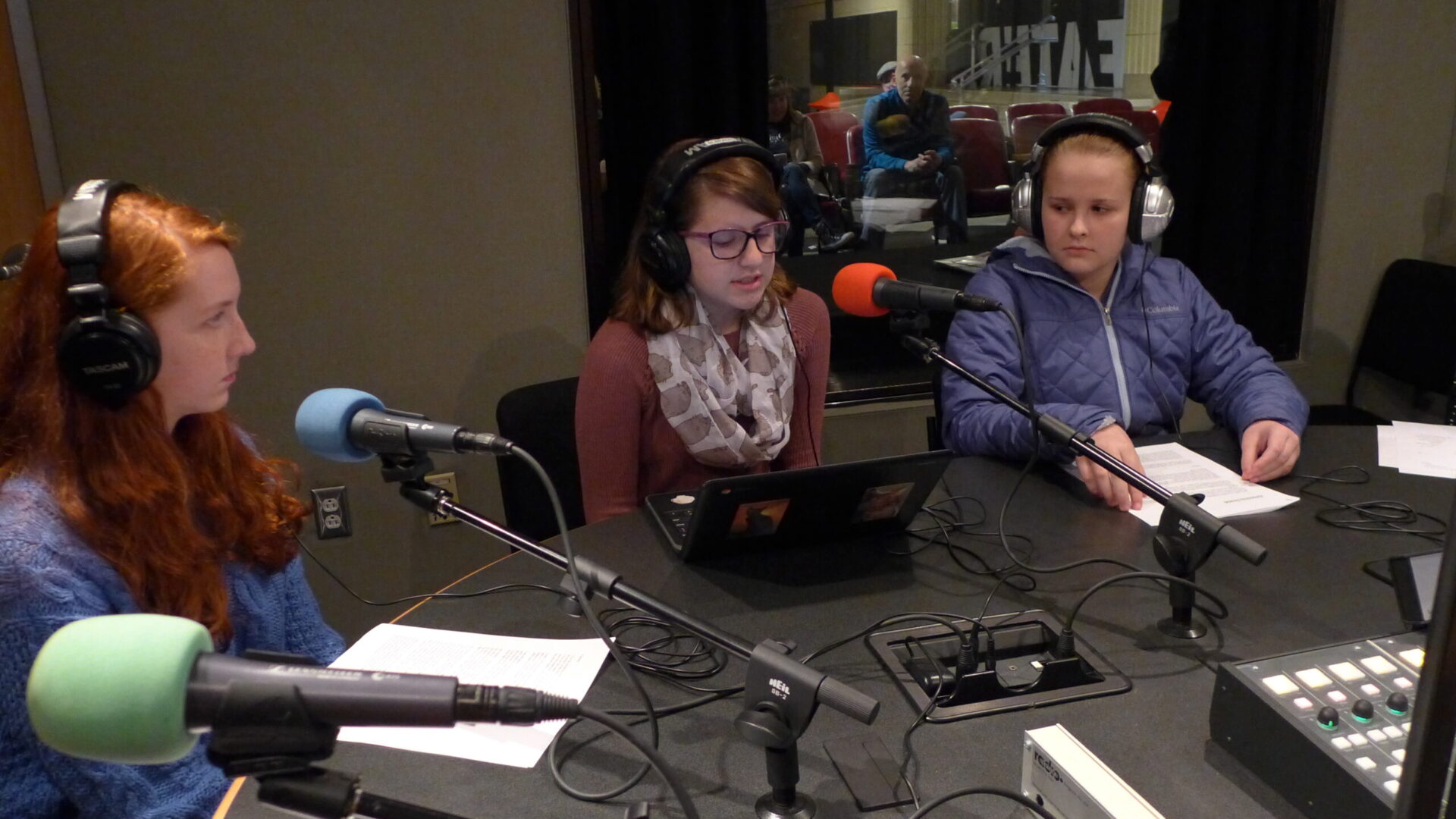 Three teens wearing headphones speaking into microphones in a radio studio