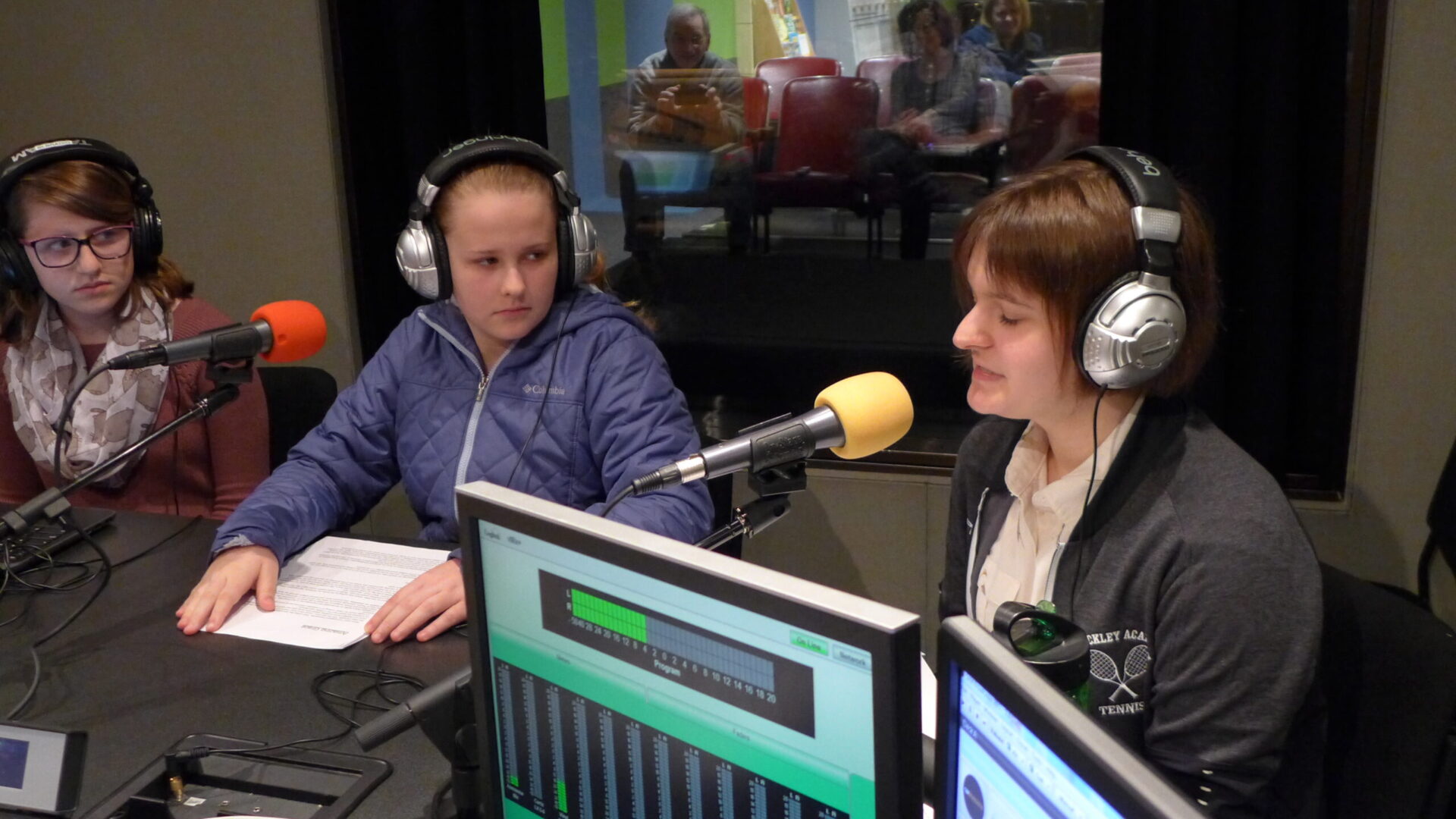 Three teens wearing headphones speaking into microphones in a radio studio