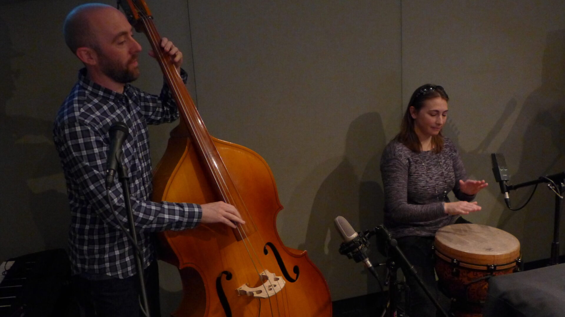 An adult playing upright bass and an adult playing a drum in a radio studio