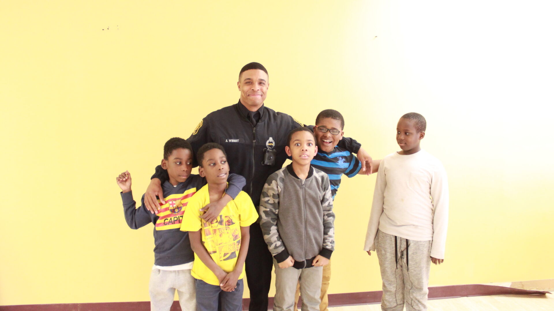 Adult wearing a police uniform and five children, all smiling and posing in profile