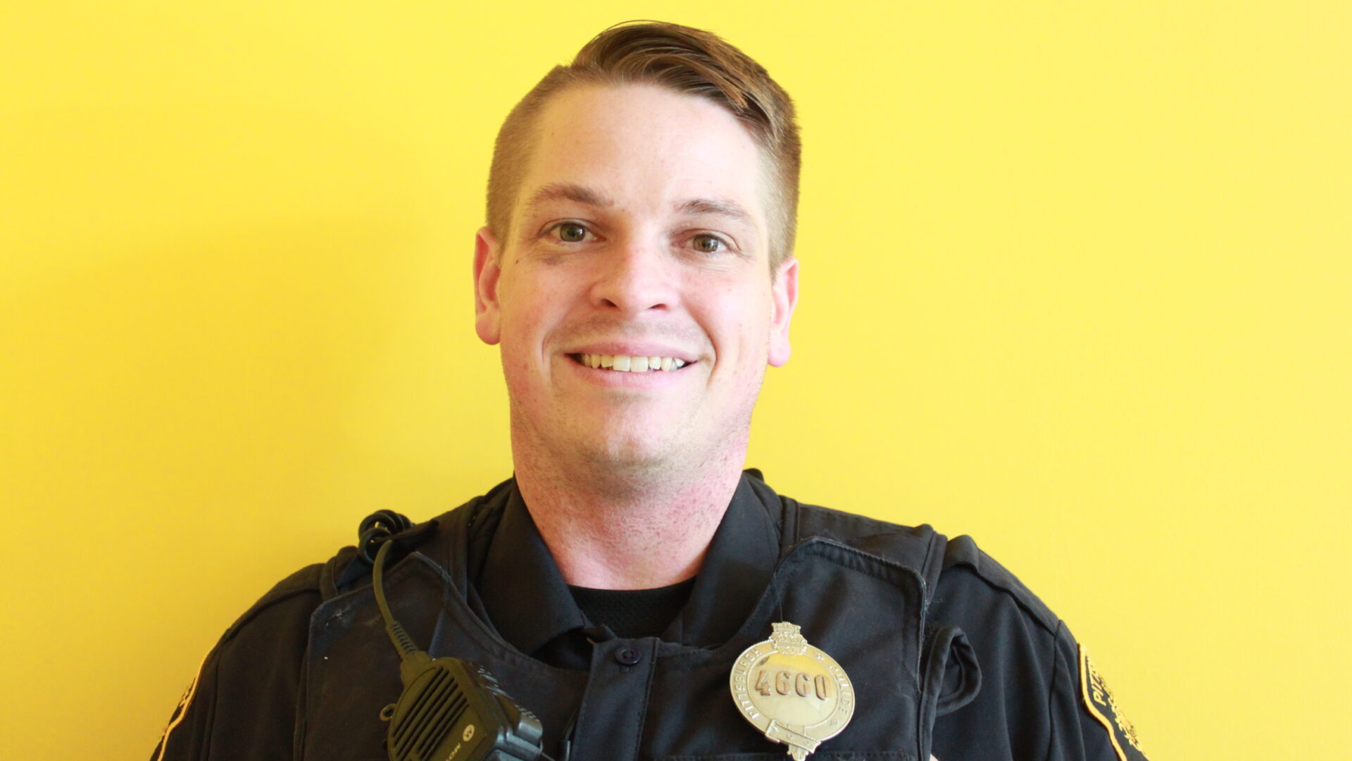 Adult with short blond hair and a police uniform smiling in profile