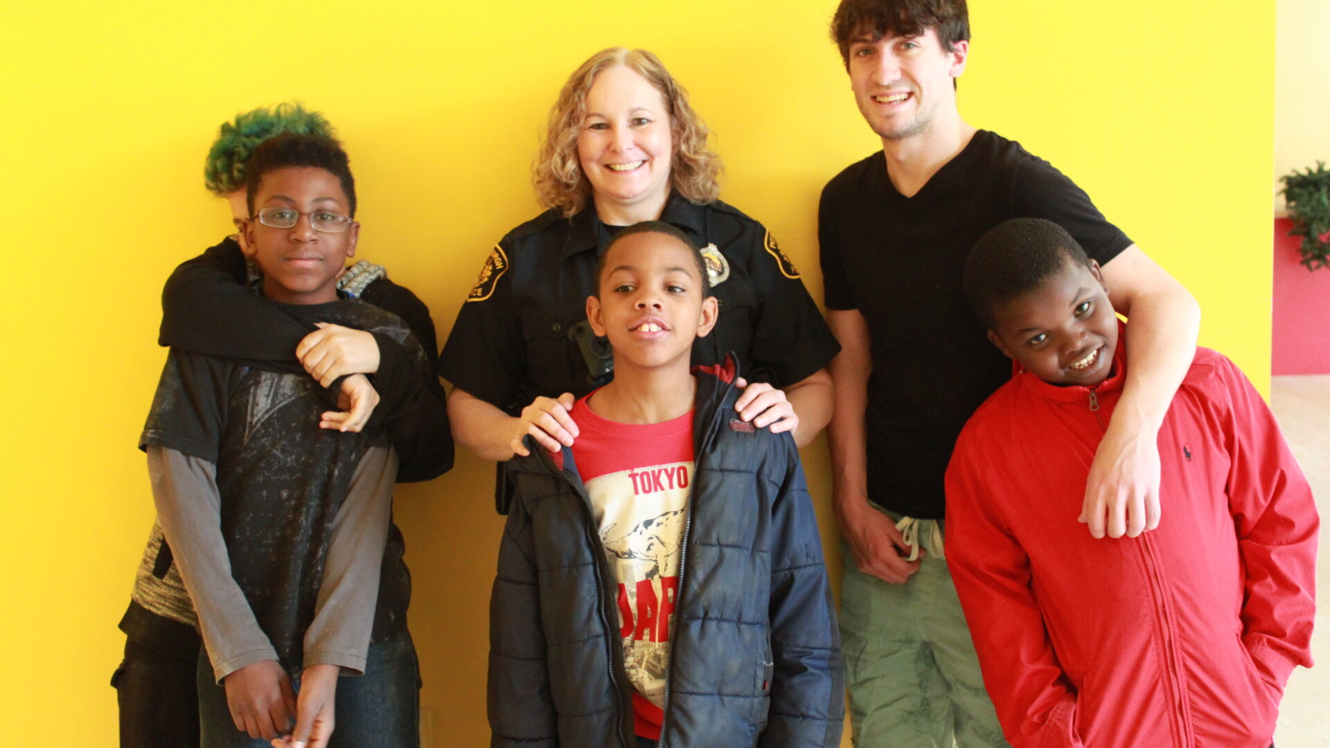 Three adults and three youth, one adult wearing a police uniform, smiling and posing in profile
