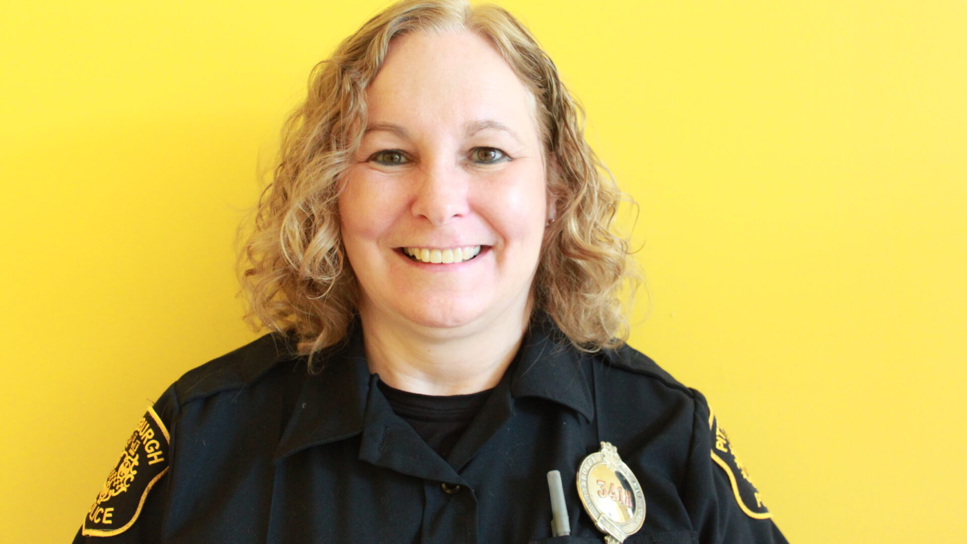 Adult with curly blond hair and a police uniform smiling in profile
