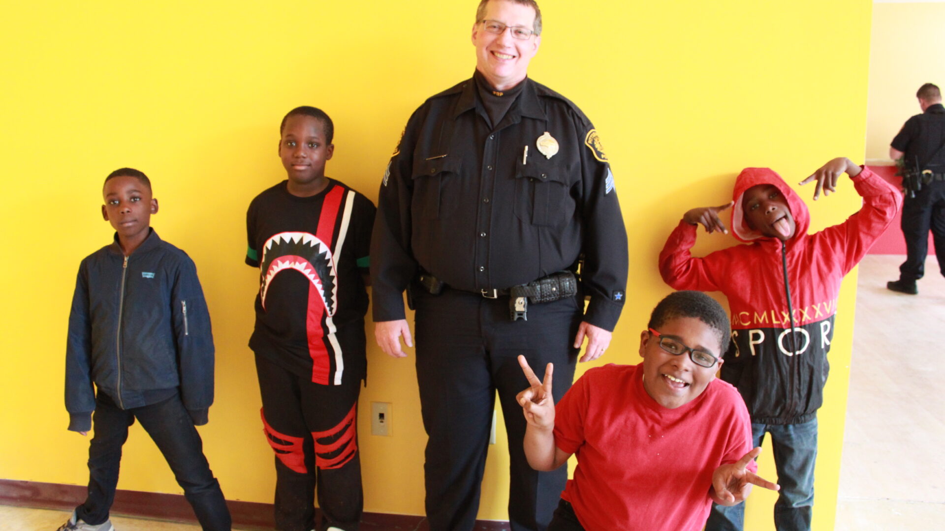One adult wearing a police uniform and four children smiling and posing in profile