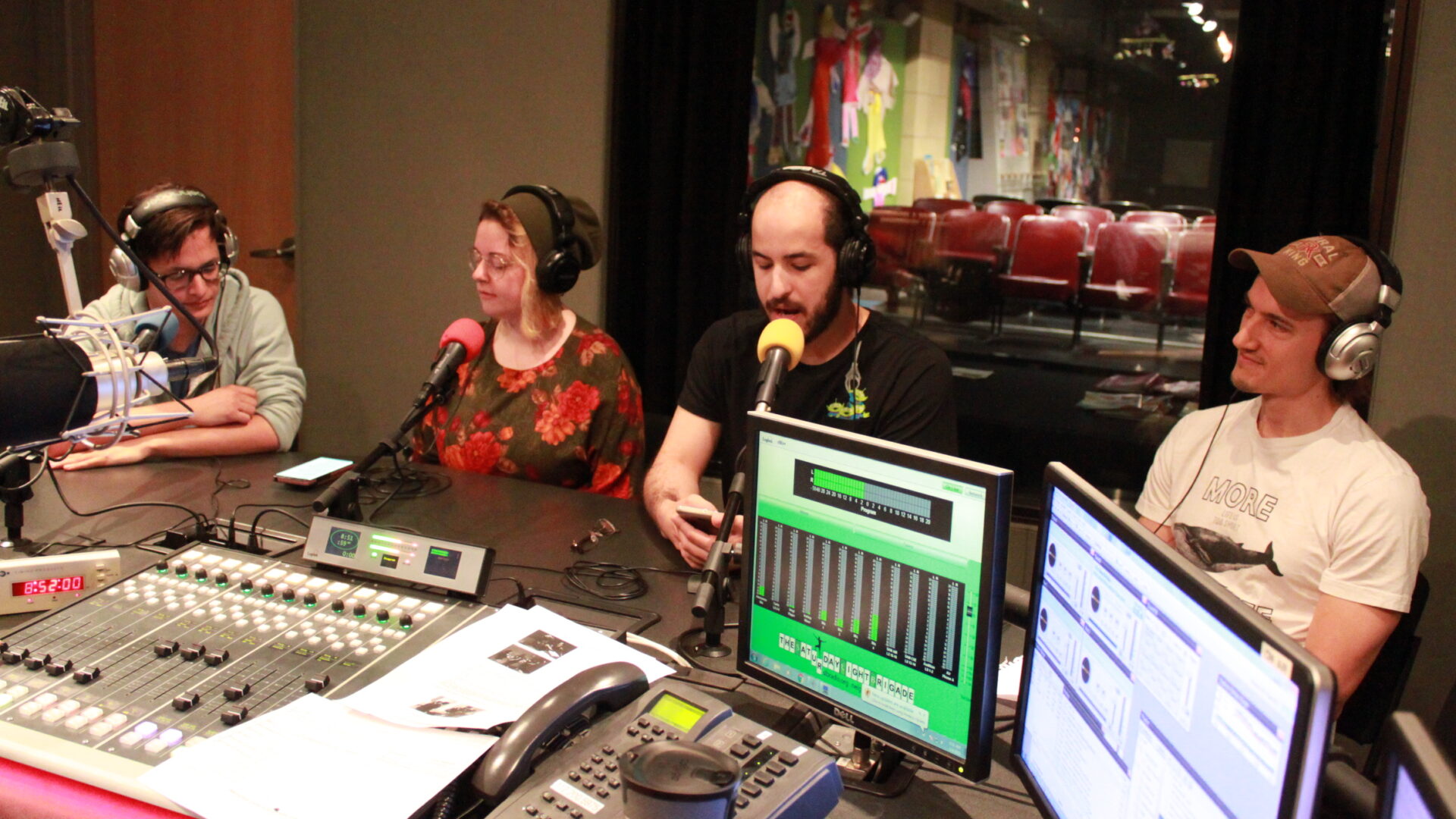Four young adults wearing headphones and speaking into microphones in a radio studio