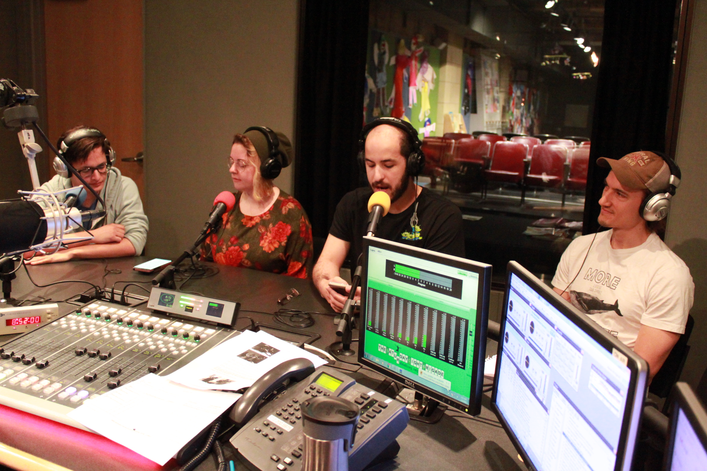Four young adults wearing headphones and speaking into microphones in a radio studio