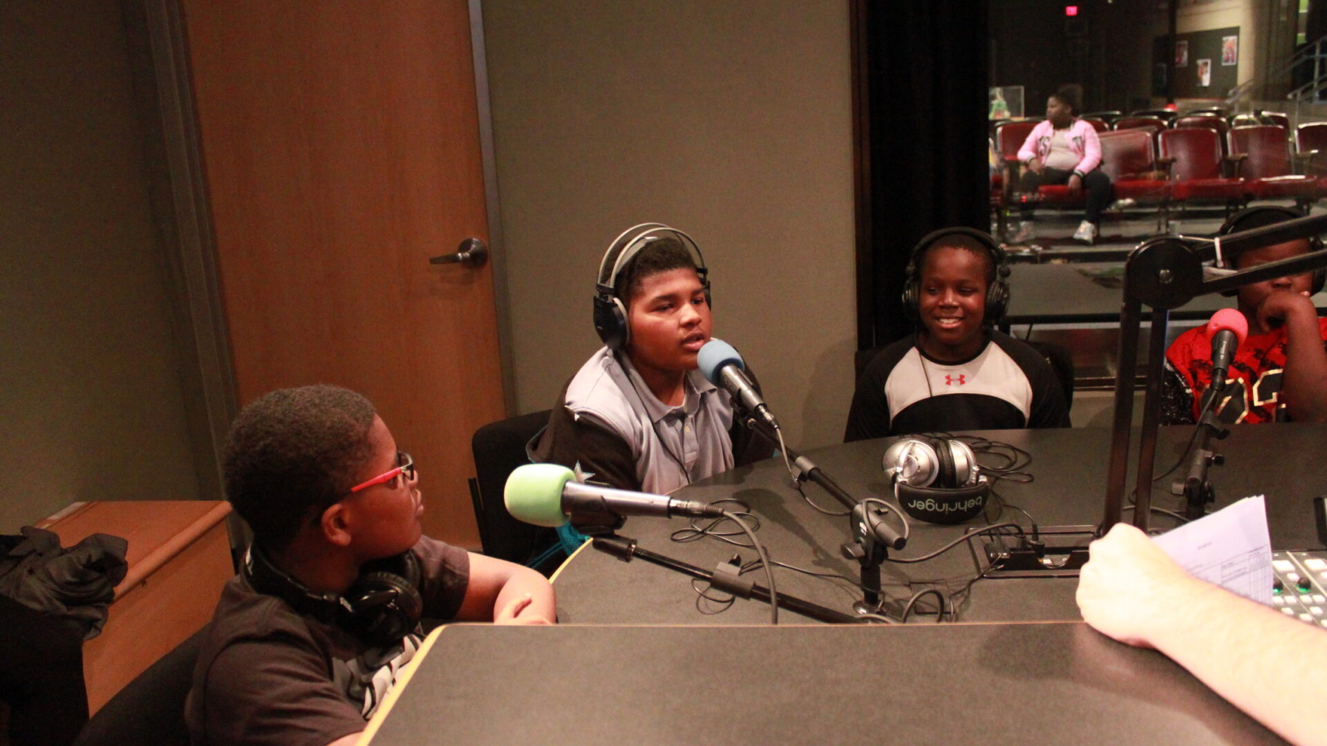 Four youth wearing headphones and speaking into microphones in a radio studio