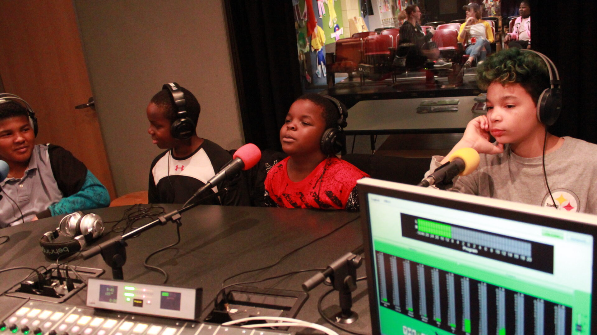 Four youth wearing headphones and speaking into microphones in a radio studio