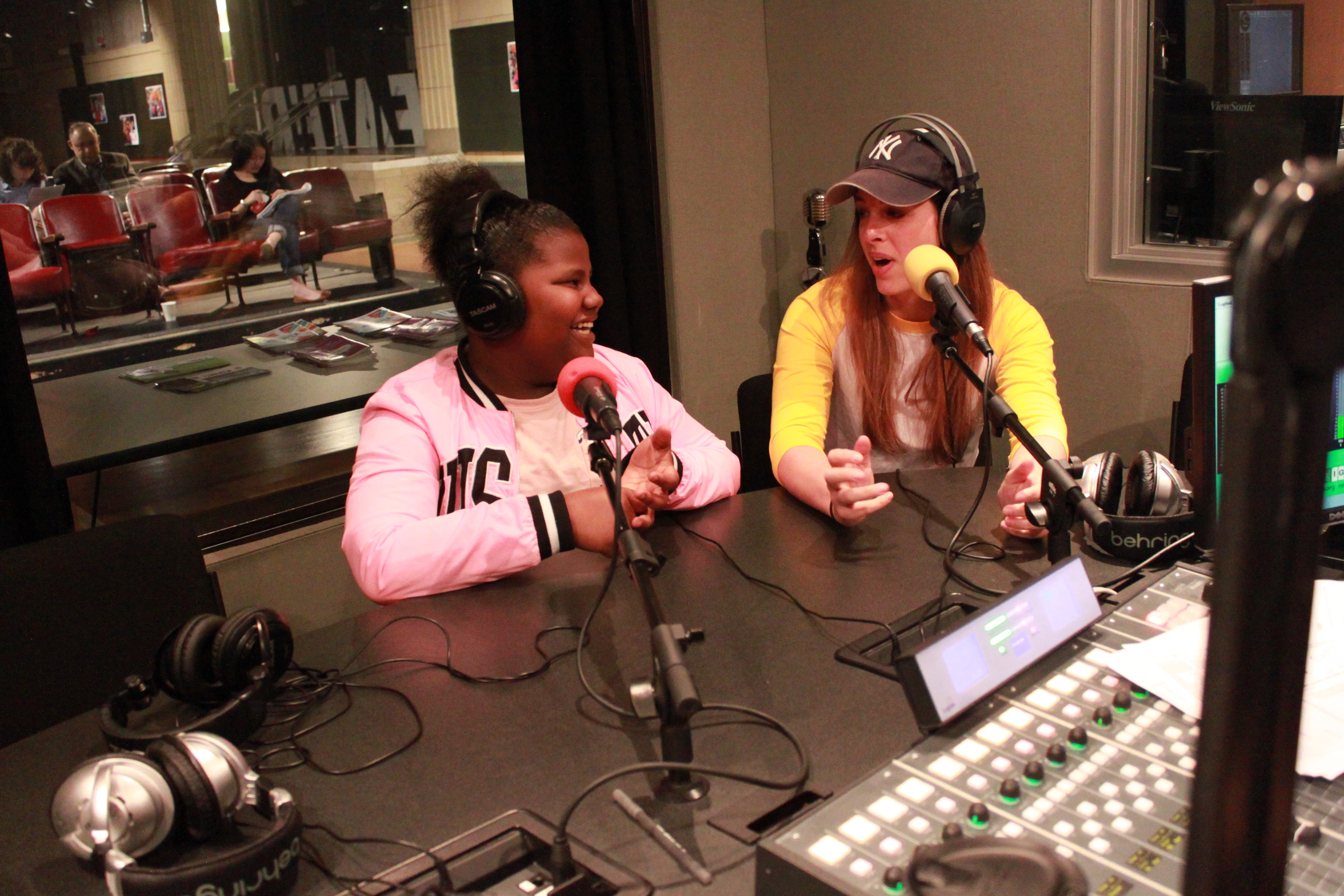An adult and a youth both wearing headphones and speaking into microphones in a radio studio