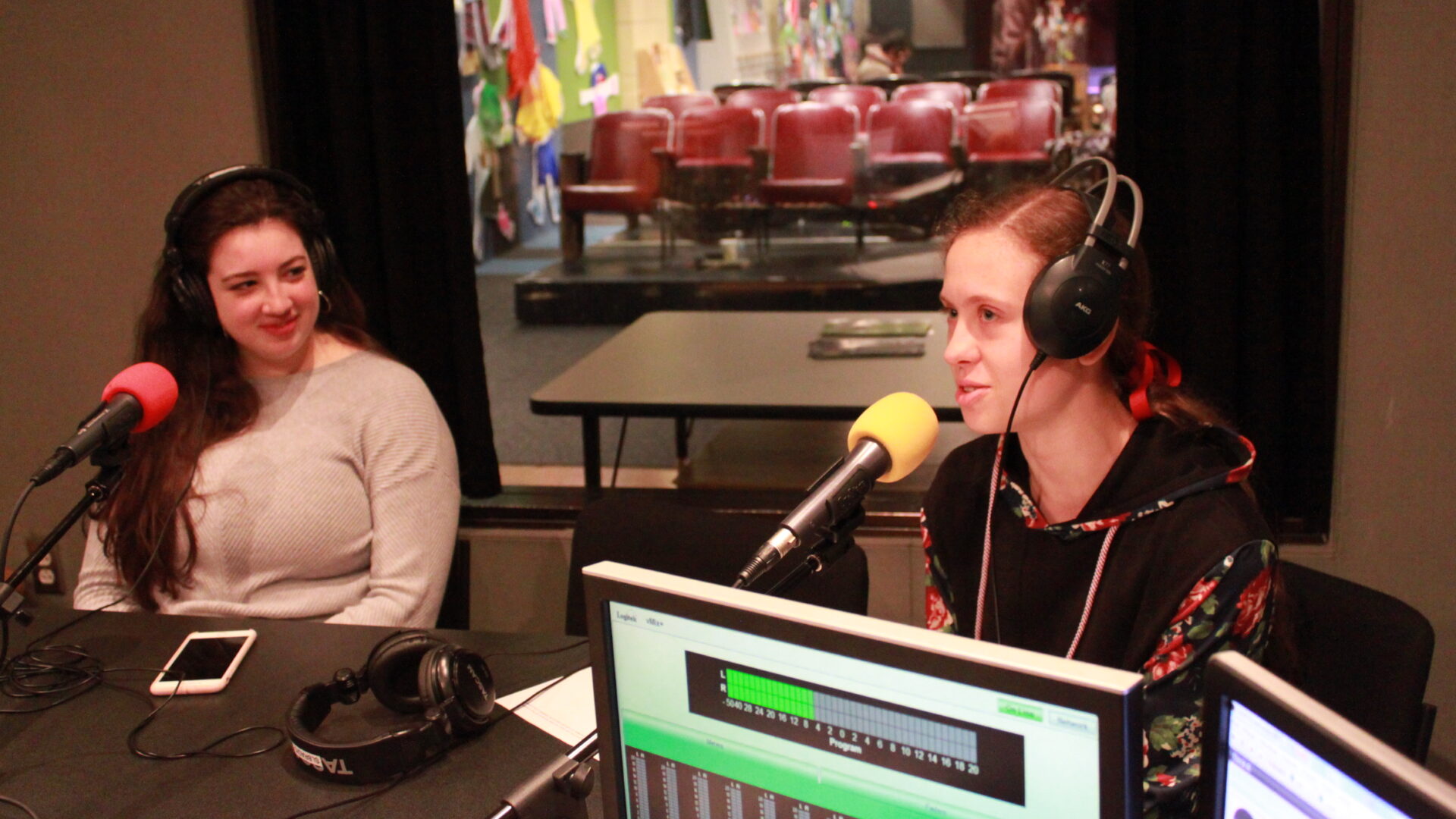 Two teens wearing headphones and speaking into microphones in a radio studio