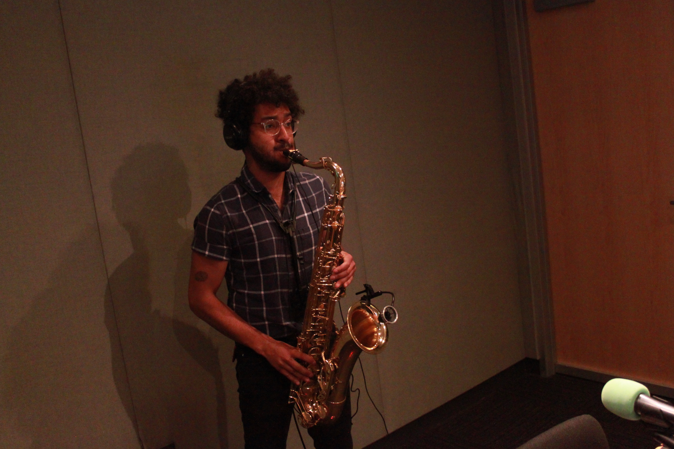 Adult wearing headphones playing tenor saxophone in a radio studio