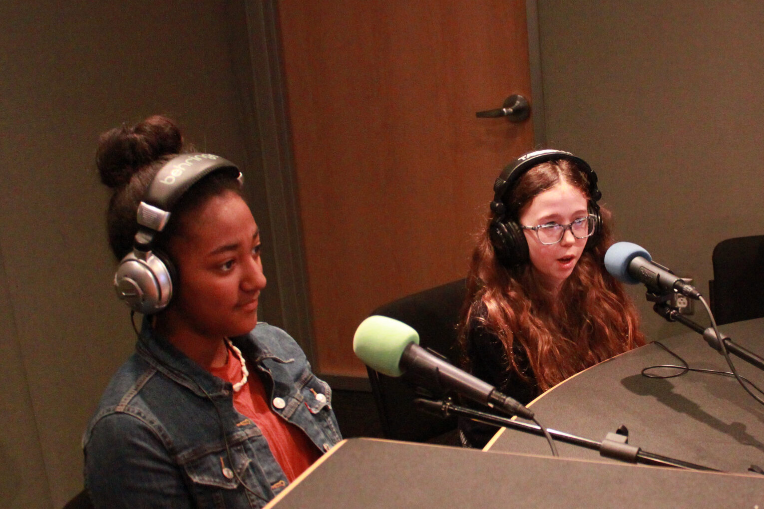 Two youth wearing headphones speaking into microphones in a radio studio