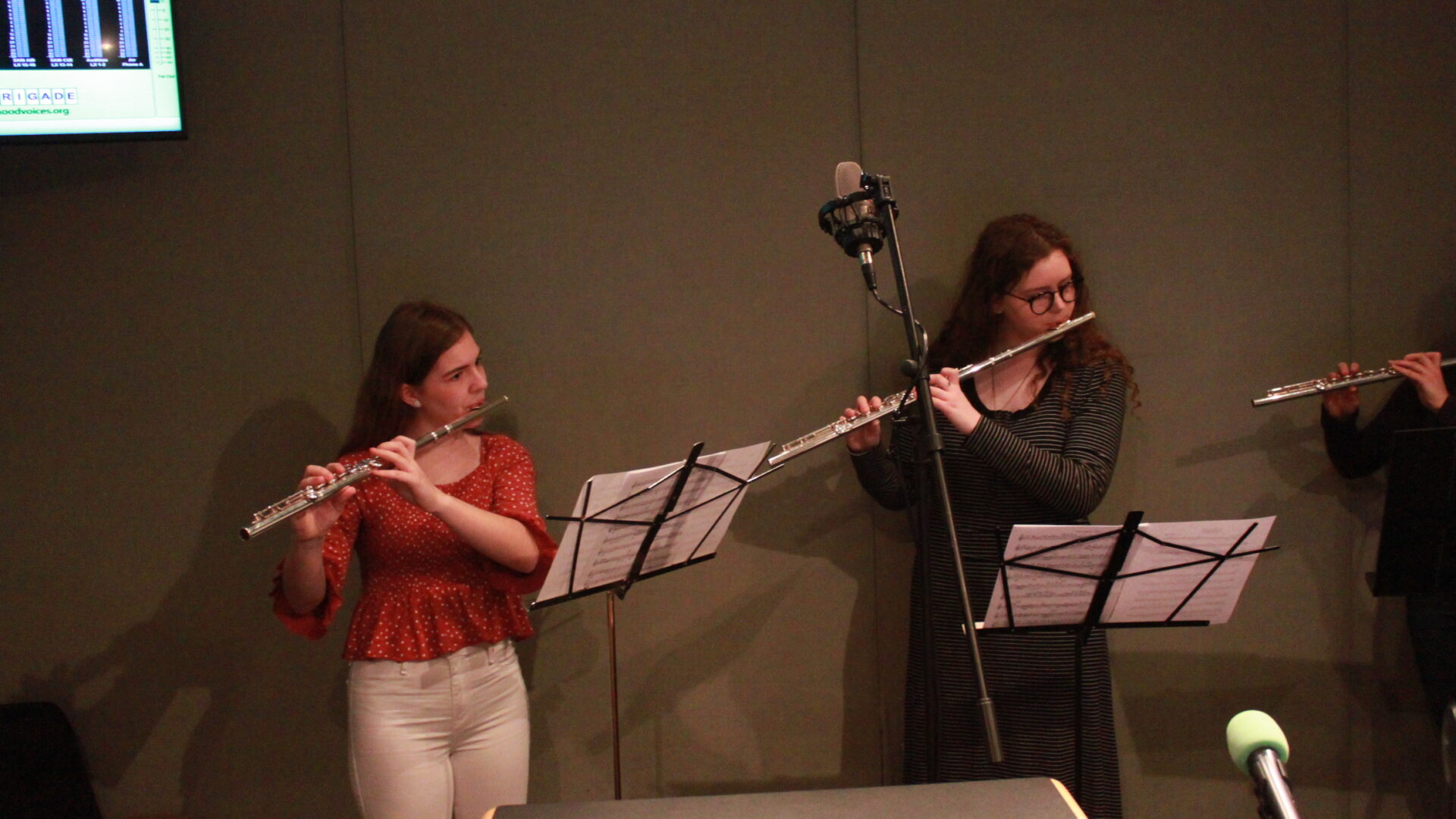 Two teens playing flute and looking at sheet music on music stands in a radio studio
