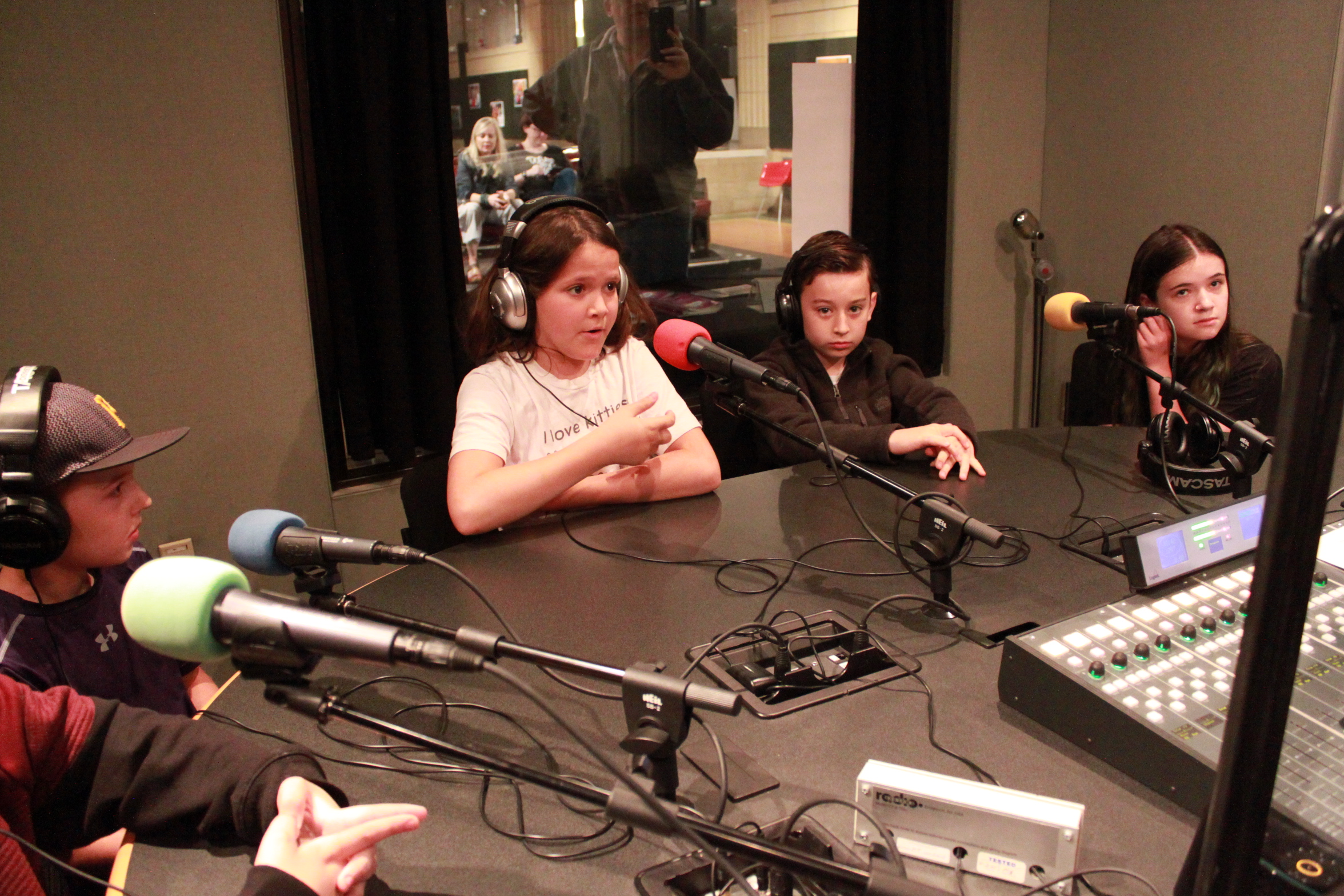 Four youth, three wearing headphones, speaking into microphones in a radio studio