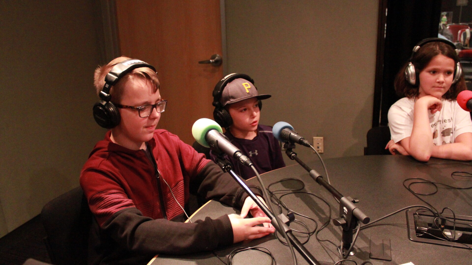 Three youth wearing headphones speaking into microphones in a radio studio