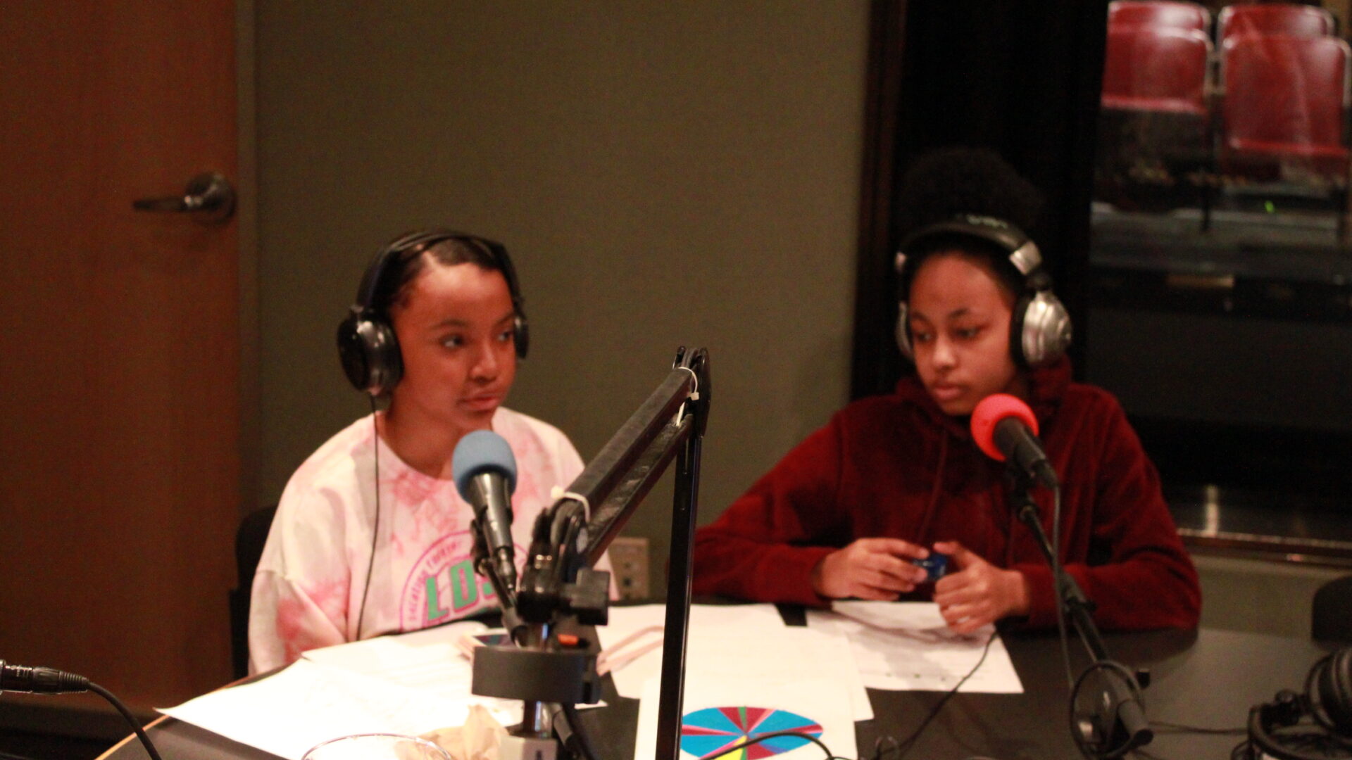 Two teen wearing headphones and speaking into microphones in a radio studio