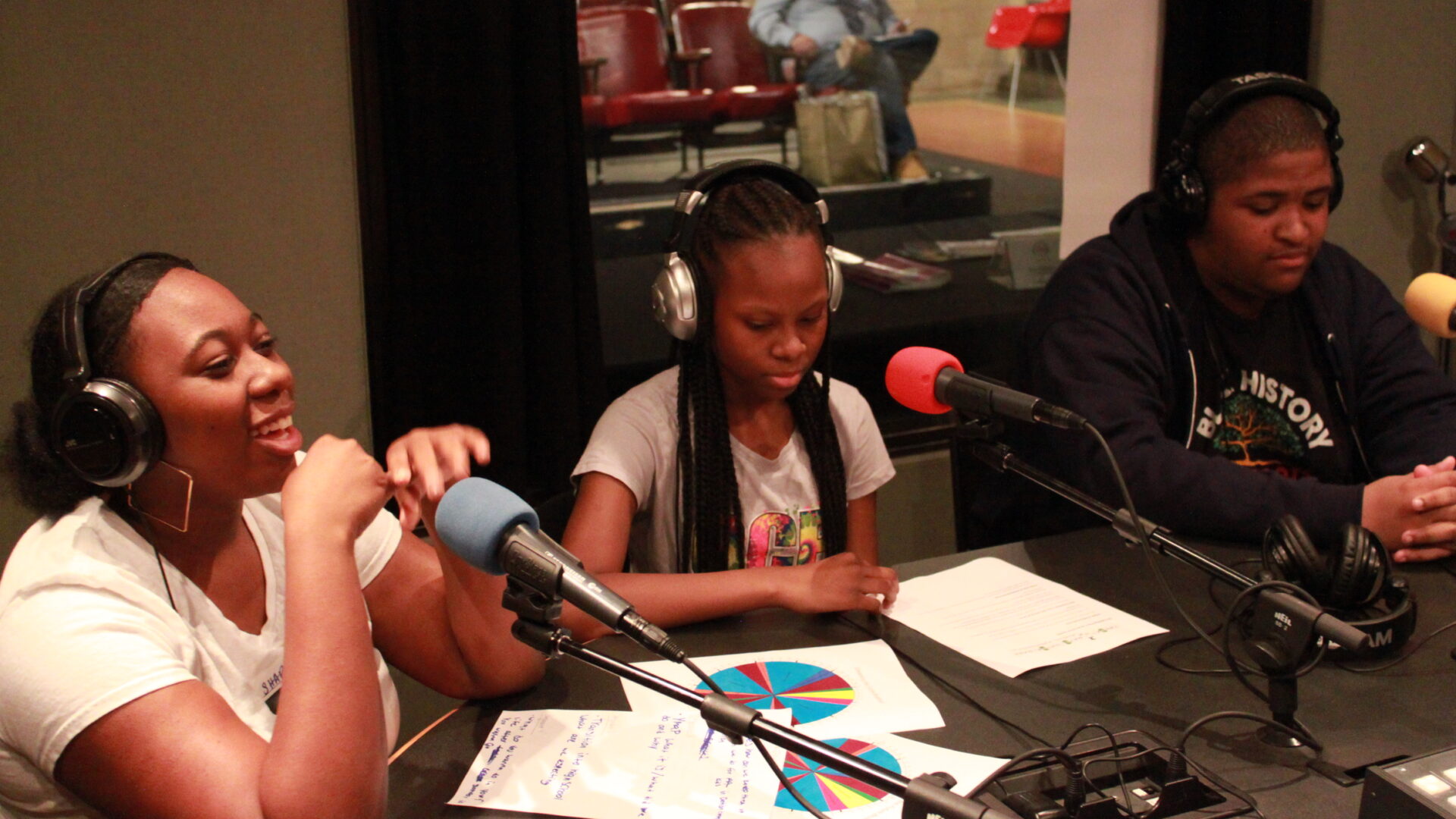 Three teens wearing headphones and speaking into microphones in a radio studio
