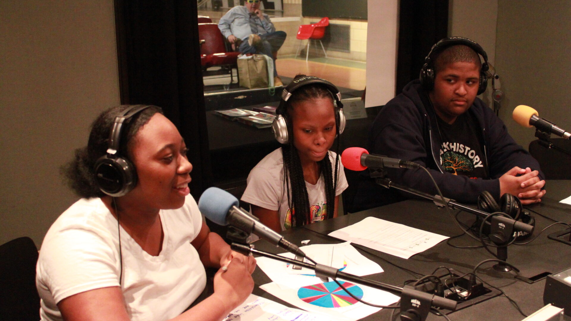Three teens wearing headphones and speaking into microphones in a radio studio