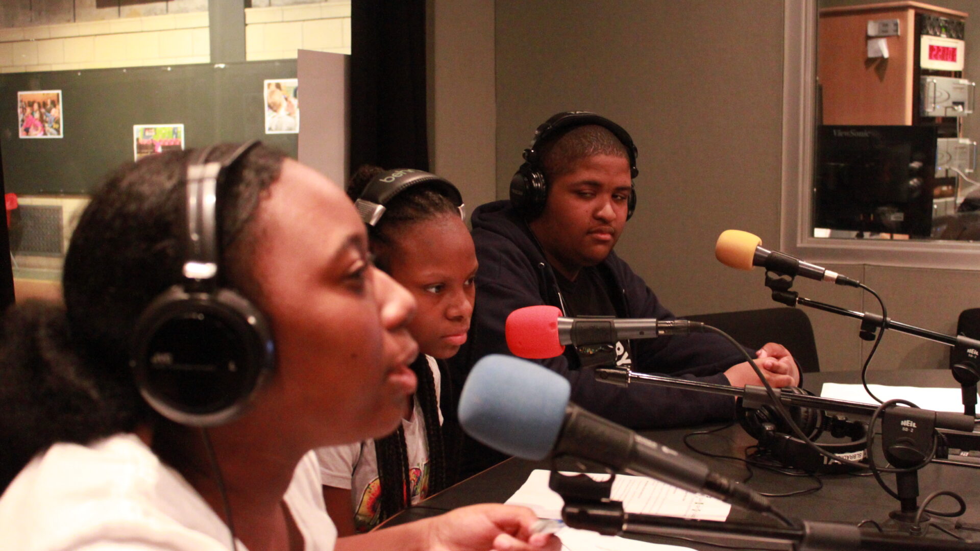 three youth wearing headphones speaking into microphones in a radio studio