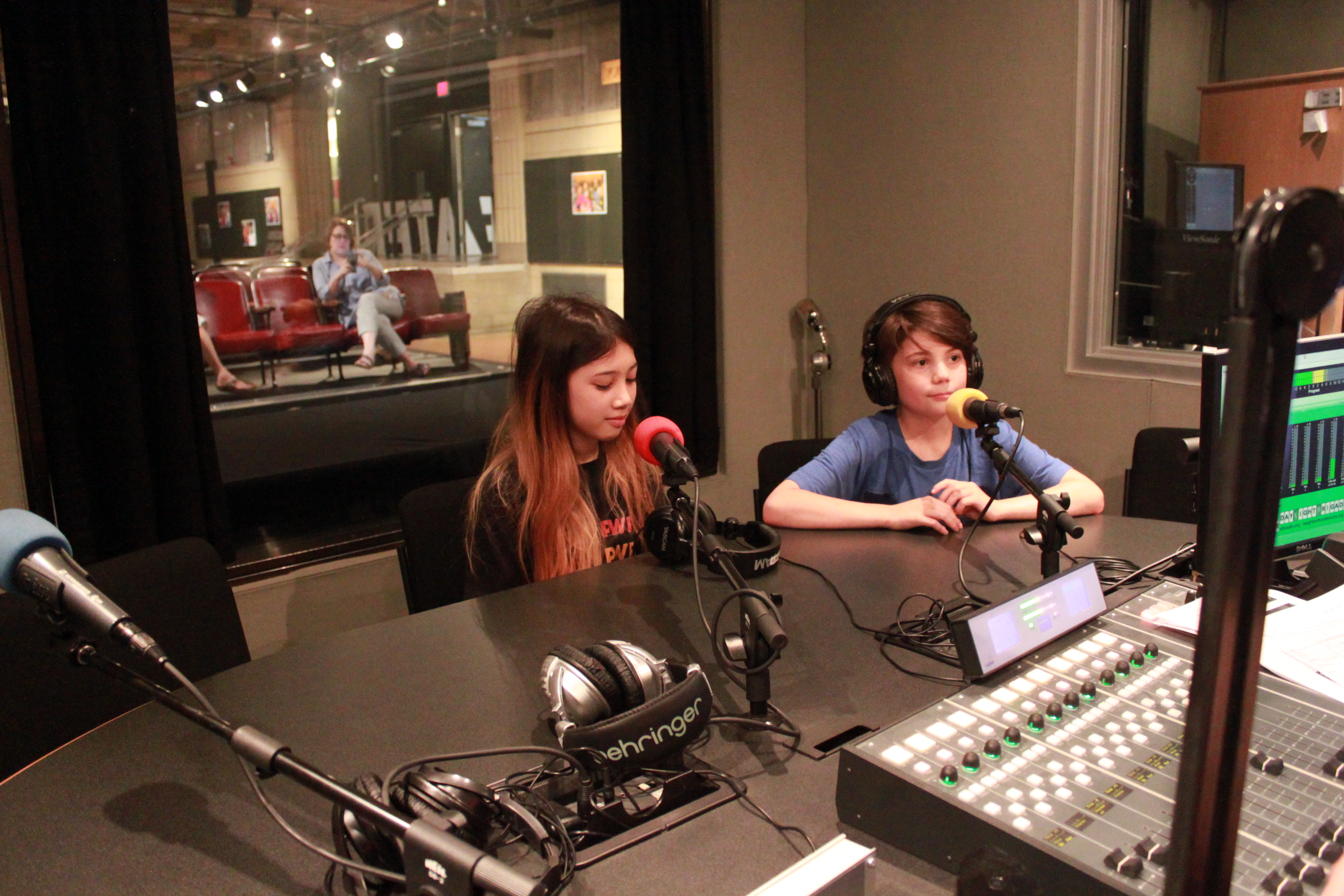 Two youth, one wearing headphones, sitting in front of microphones in a radio studio