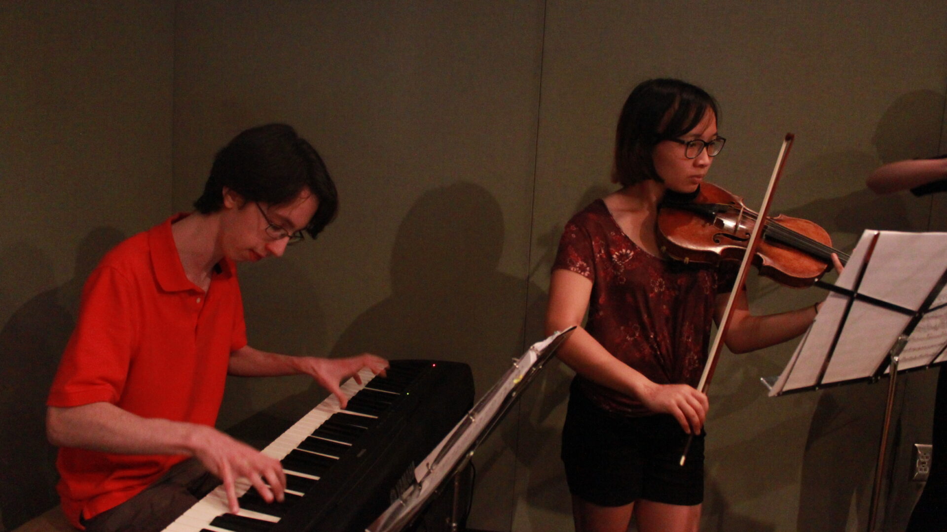 Two youth performing on piano keyboard and violin looking at sheet music on music stands in a radio studio