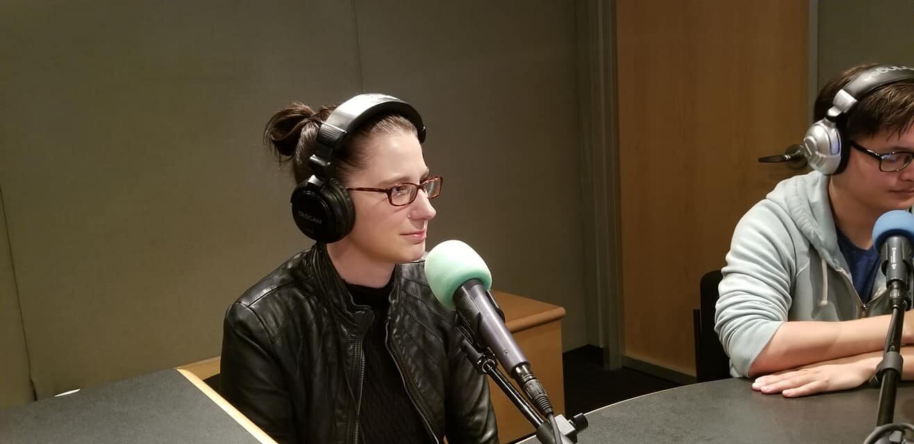 Two teens wearing headphones sitting in front of microphones in a radio studio