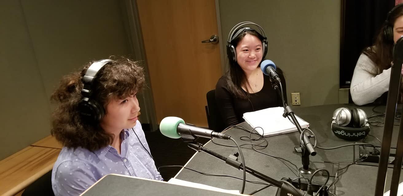 Three teens wearing headphones sitting in front of microphones in a radio studio