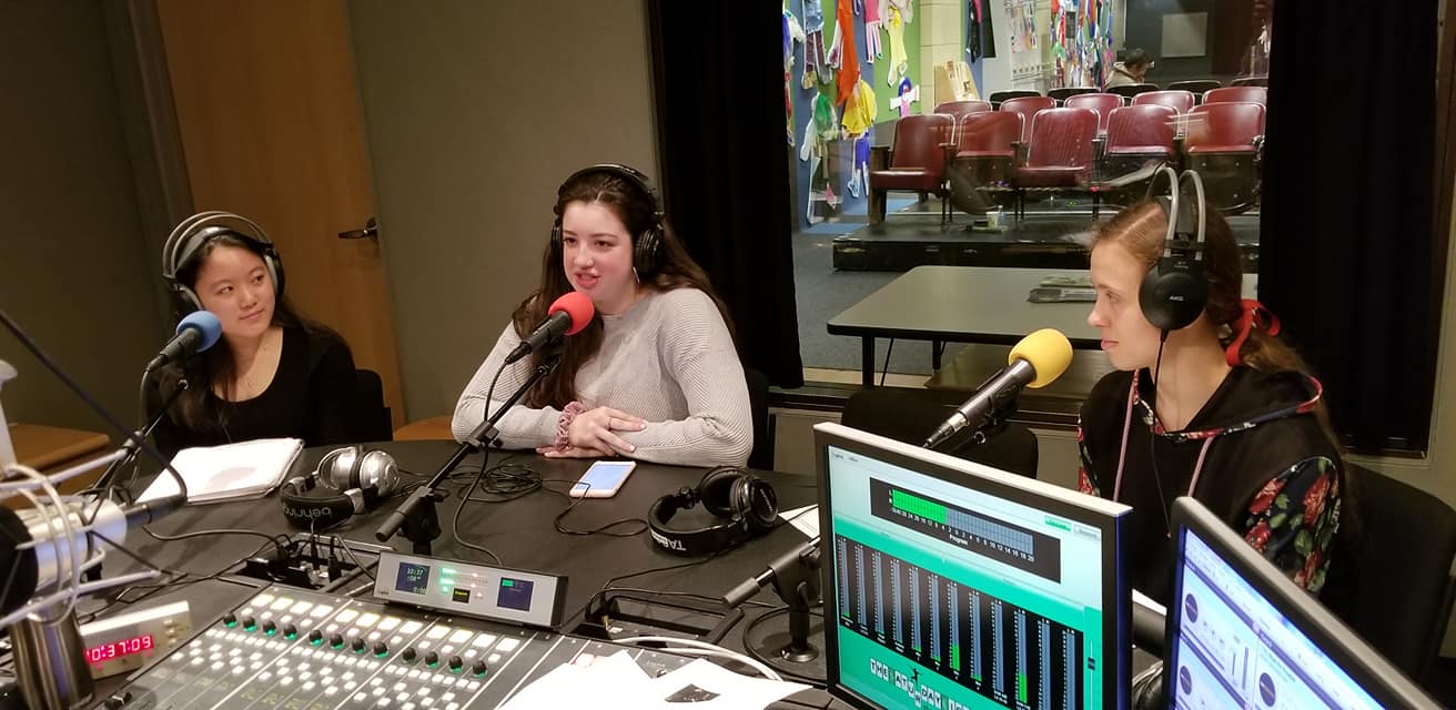 Three teens wearing headphones and speaking into microphones in a radio studio