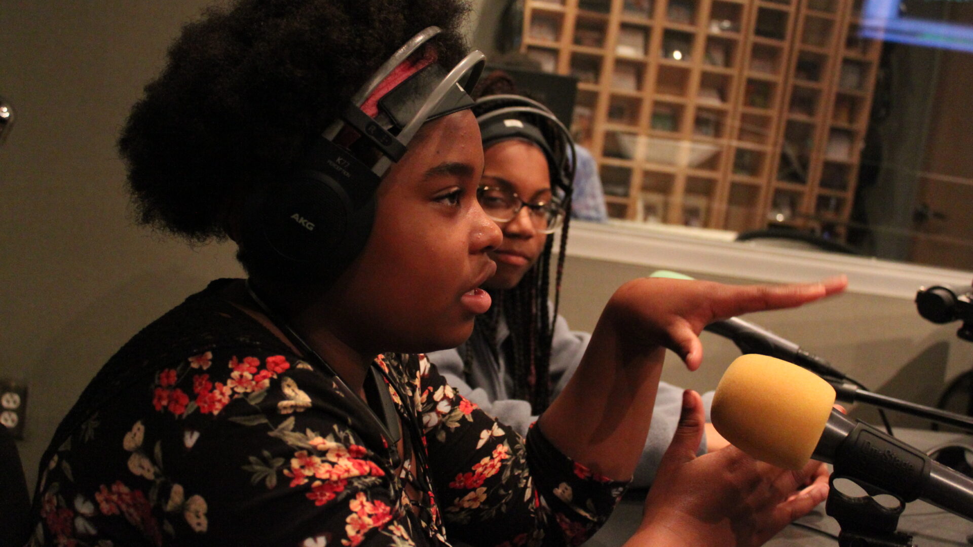 Two teens wearing headphones and speaking into microphones in a radio studio