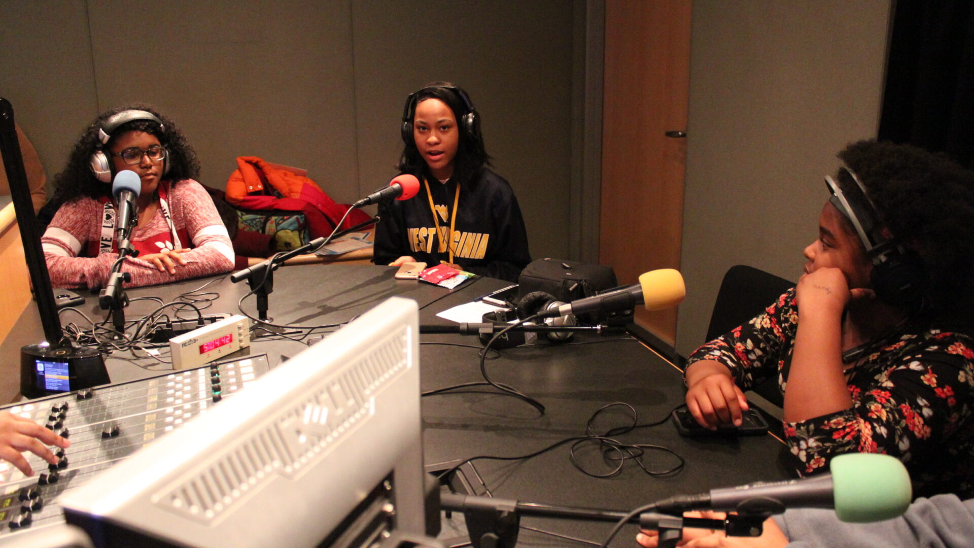 Three teens wearing headphones and speaking into microphones in a radio studio