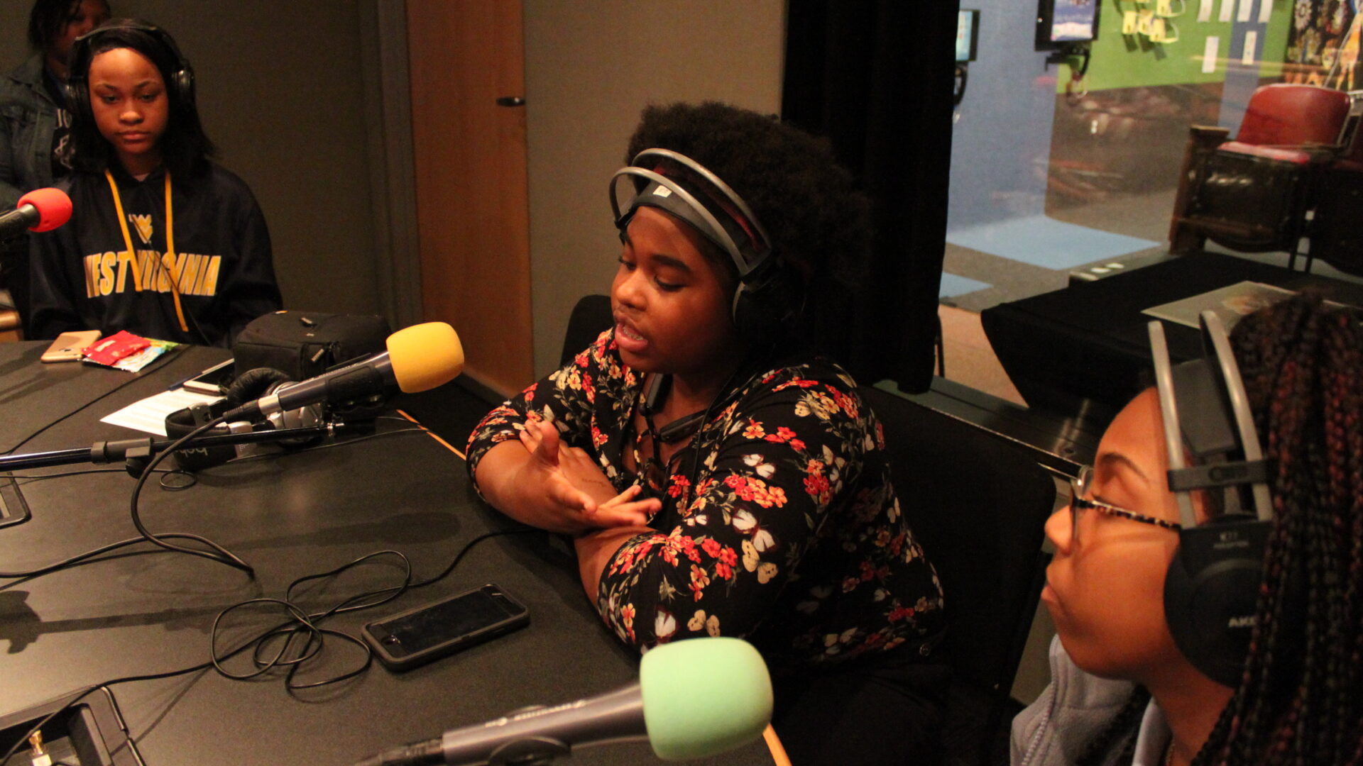 Three teens wearing headphones and speaking into microphones in a radio studio