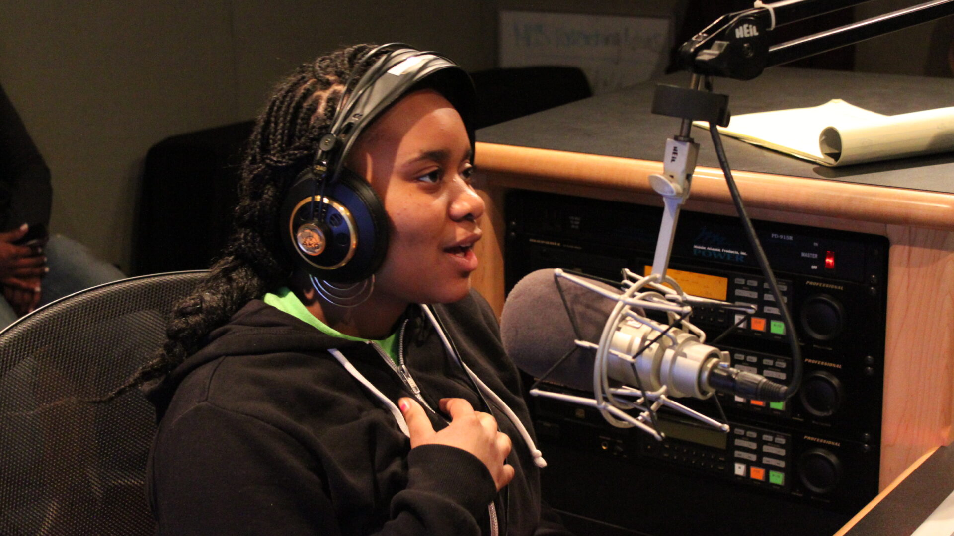 Teen wearing headphones speaking into a microphone in front of a mixing board in a radio studio
