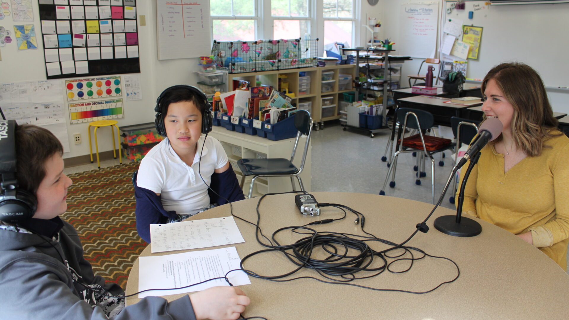 Two youth wearing headphones interviewing an adult speaking into a microphone connected to a portable recorder