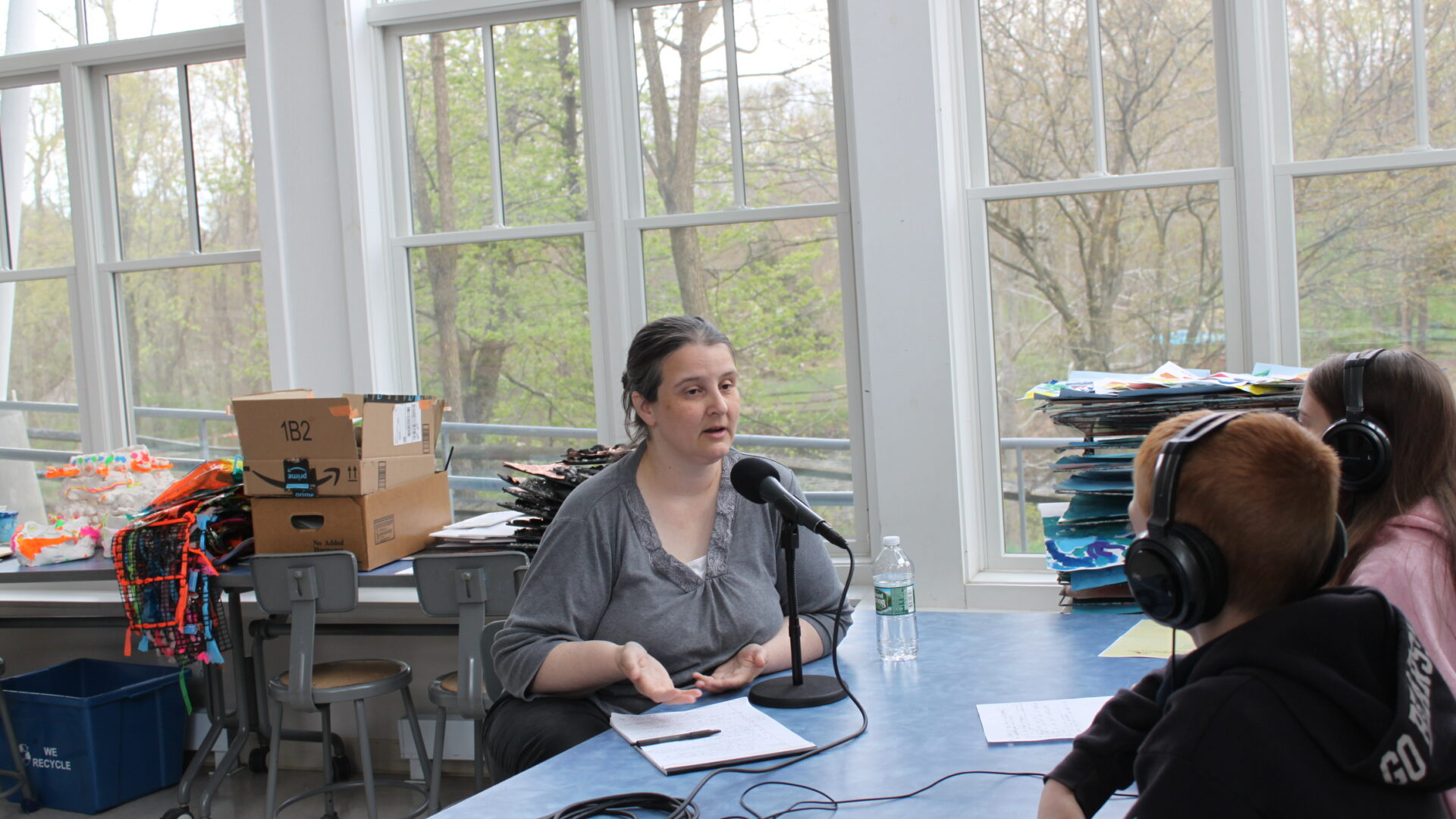 Two youth wearing headphones interviewing an adult speaking into a microphone connected to a portable recorder