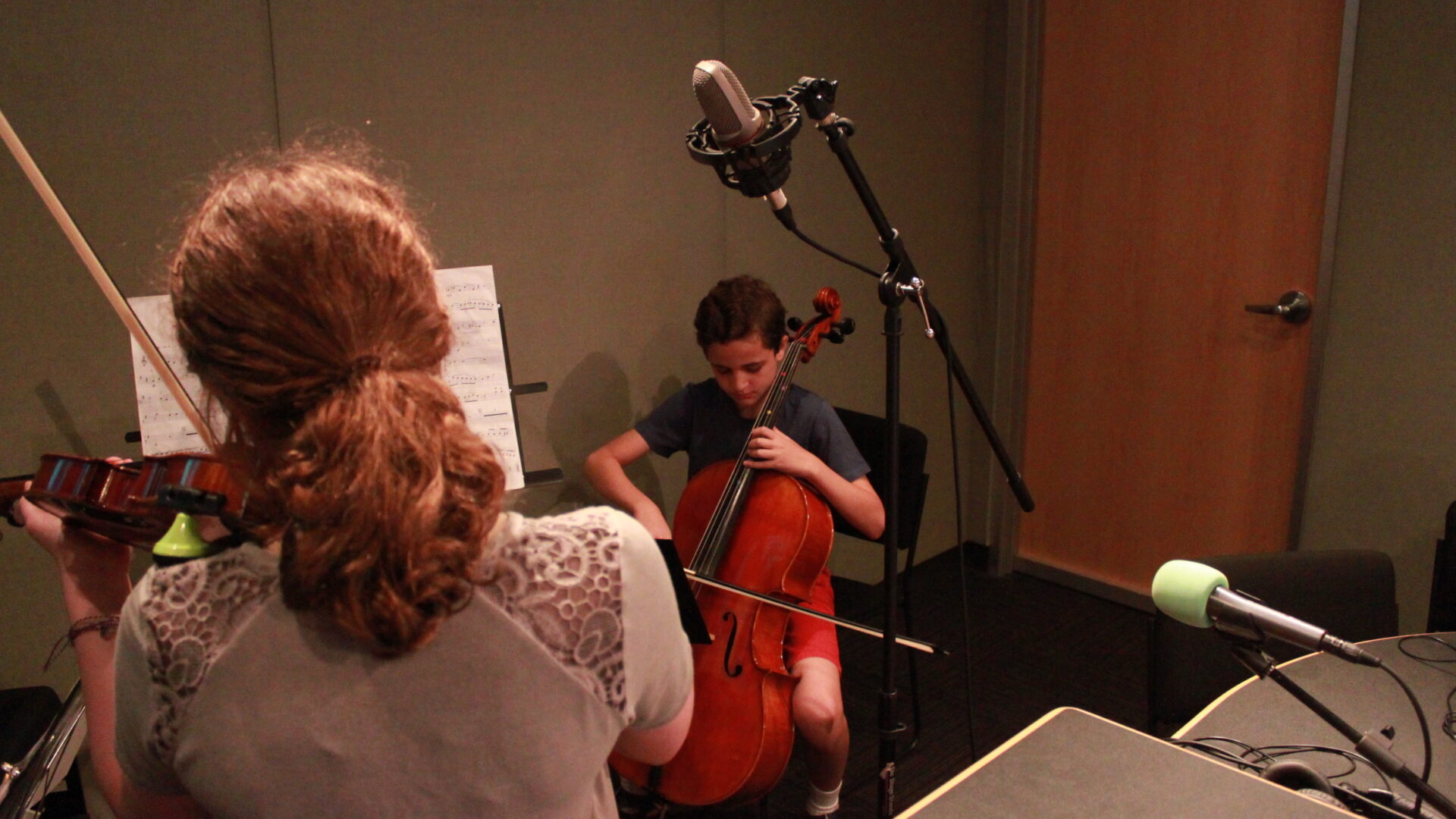 Two youth performing on violin and cello looking at sheet music on music stands in a radio studio