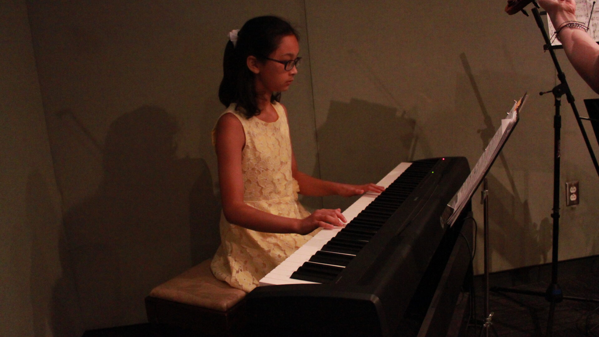 A child playing a piano keyboard looking at sheet music on a music stand in a radio studio