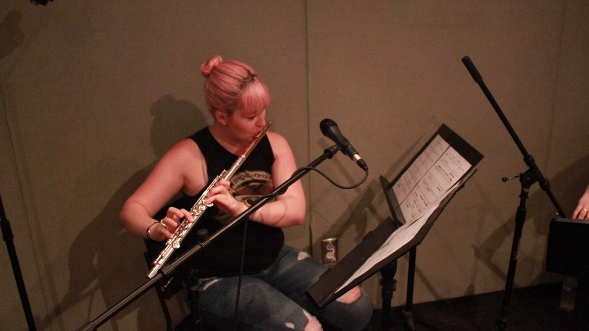 Young adult playing flute and looking at sheet music on a music stand in a radio studio