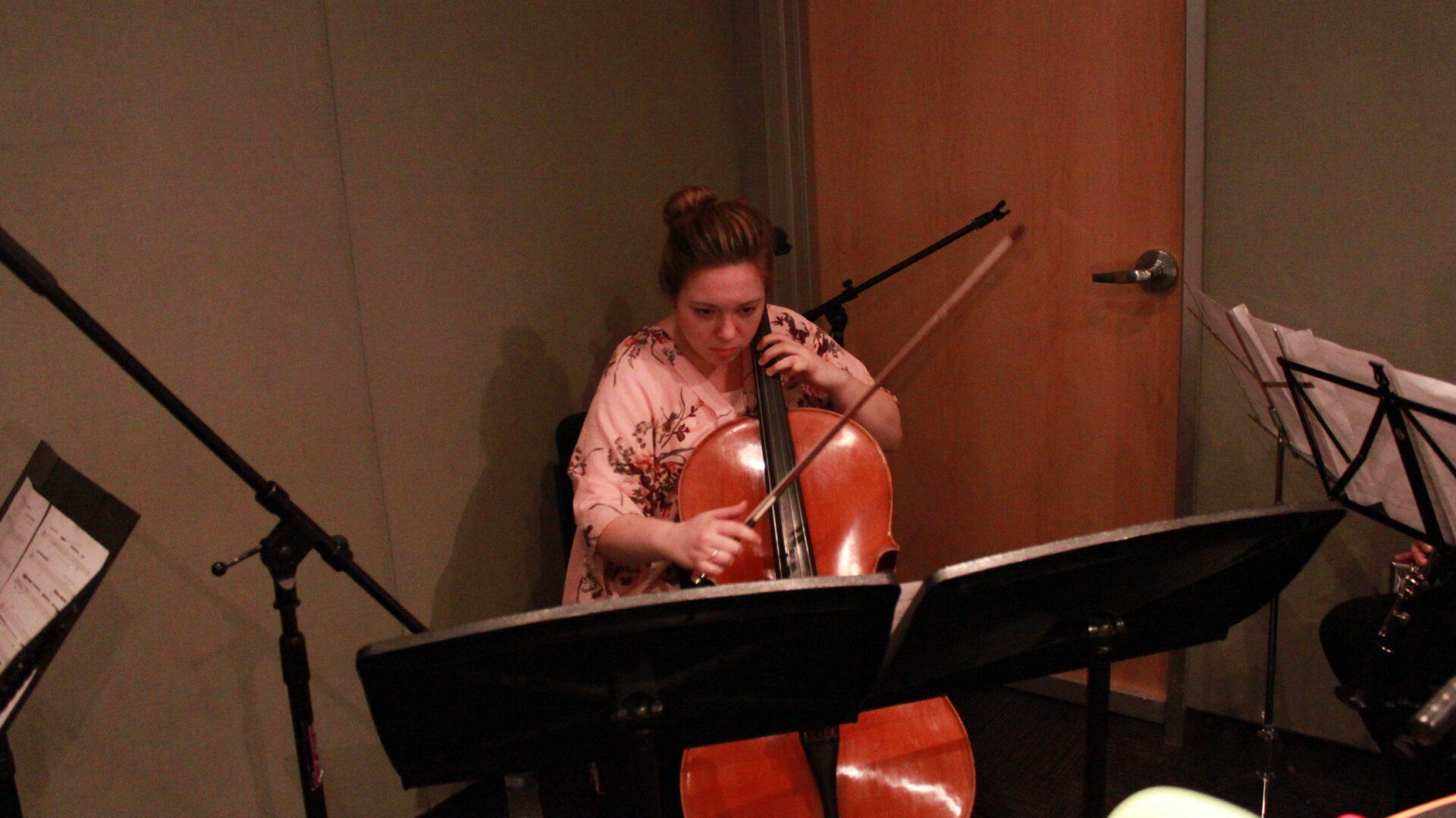 Young adult playing cello and looking at sheet music on a music stand in a radio studio