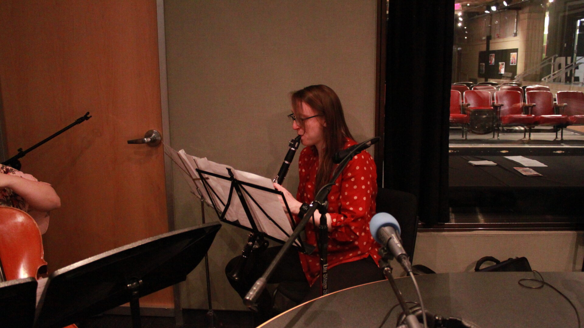 Young adult playing clarinet and looking at sheet music on a music stand in a radio studio