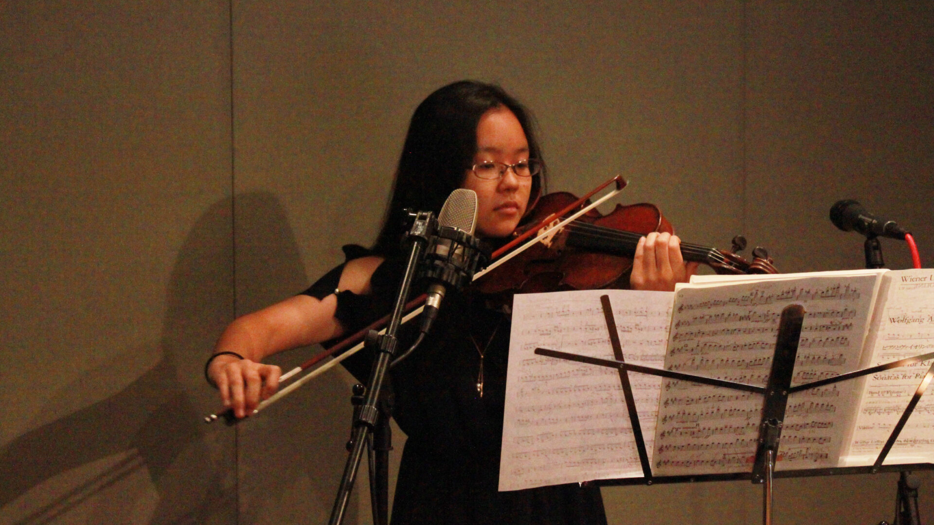 Youth playing violin looking at sheet music on a music stand in a radio studio